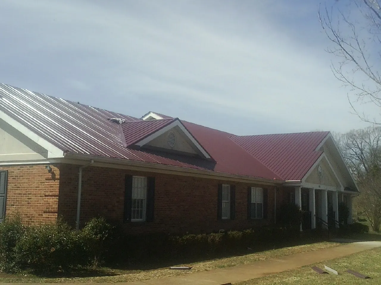 Red metal roof with gabled entries on a long brick building, from a Hail Damage Roof Repair job in Oceanside